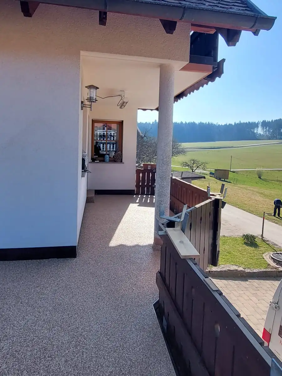 Nachher: Balkon mit Säule und Holzgeländer – von rissigem Beton zu hellem Steinteppich