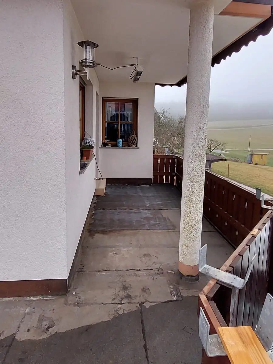 Vorher: Balkon mit Säule und Holzgeländer – von rissigem Beton zu hellem Steinteppich