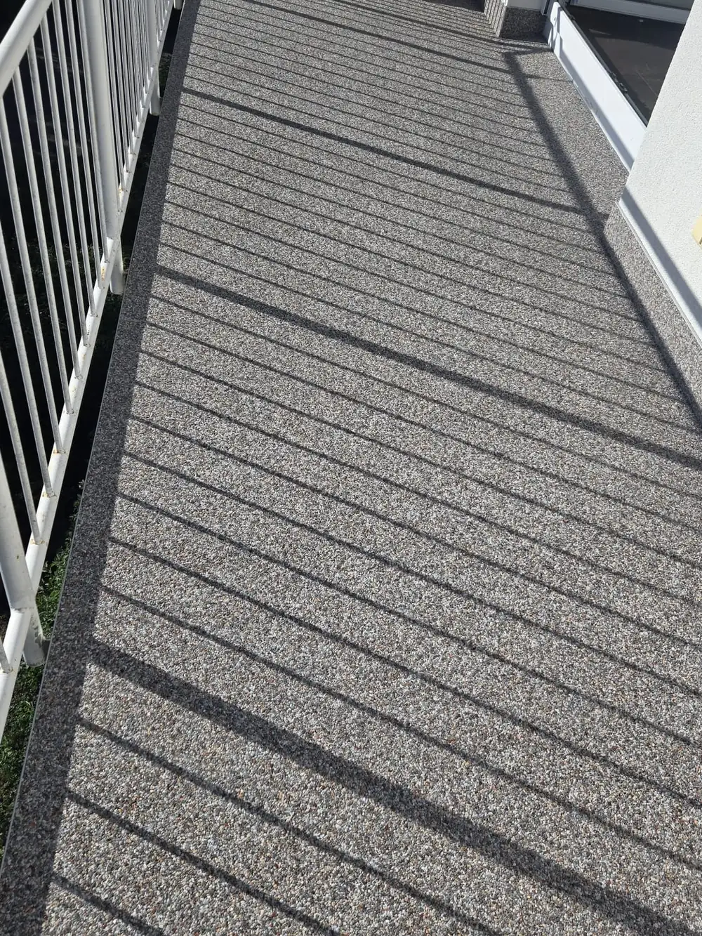 Balkon mit grauem Steinteppich und Schattenwurf des Geländers