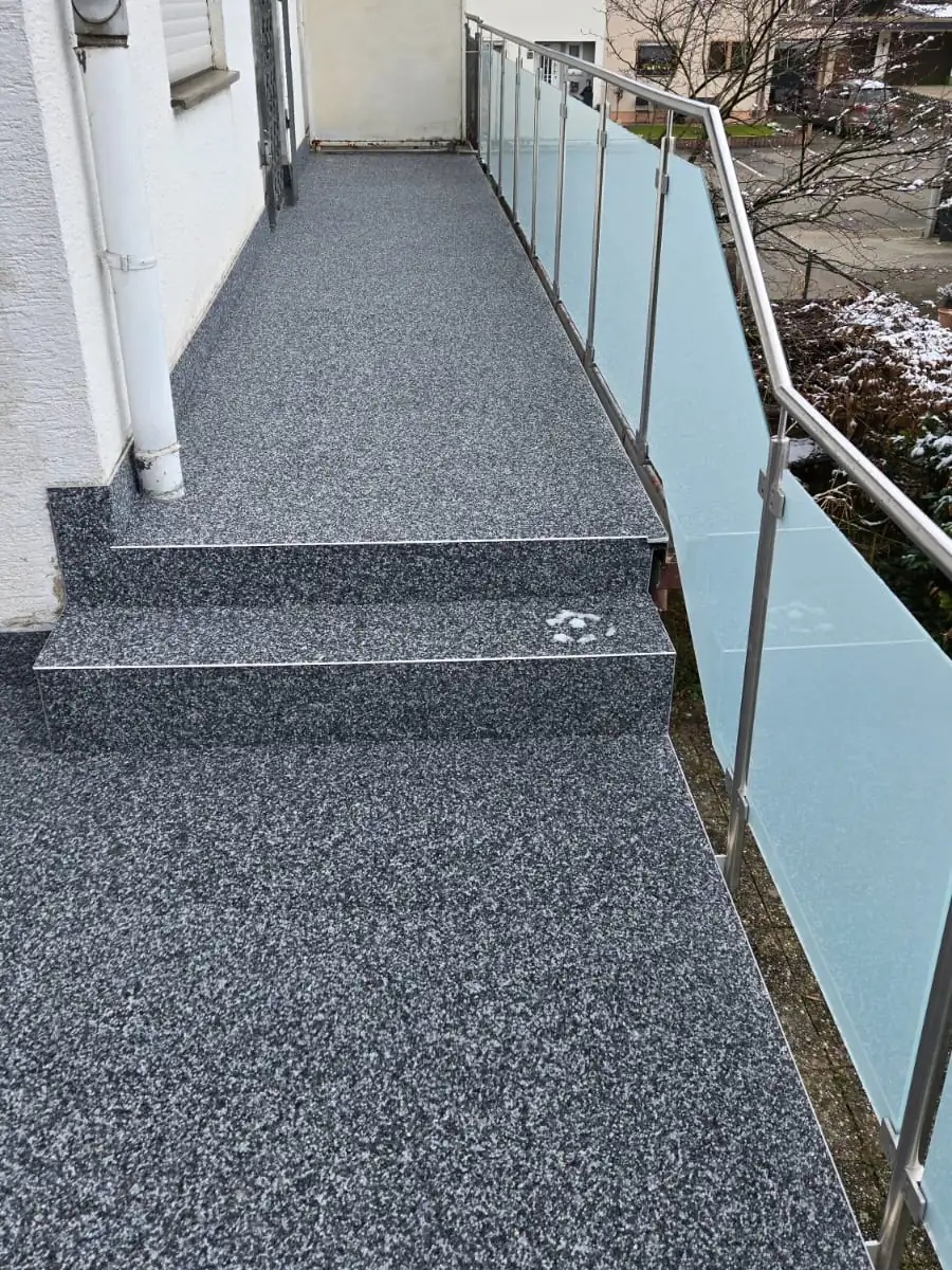 Balkon mit Stufe und Glasgeländer, fugenlos mit Steinteppich belegt
