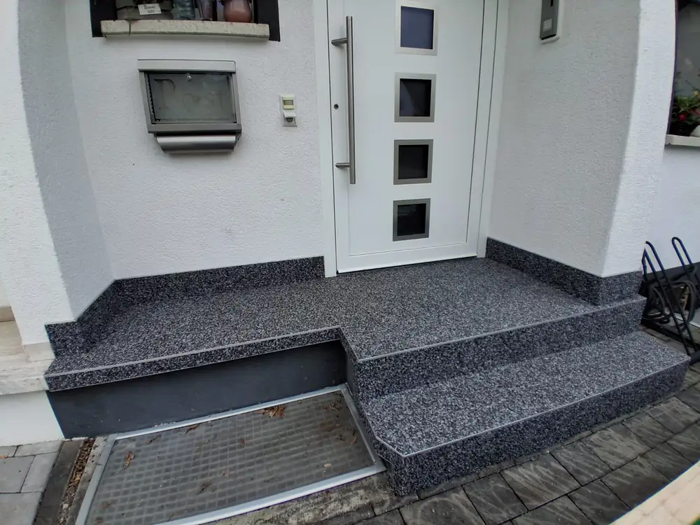Nachher: Eingangspodest aus Beton – mit dunklem Steinteppich und Sockelkante